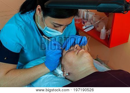 Correction of the shape of the eyebrows in the beauty salon. The doctor is a cosmetologist at work. Technique of microblading.