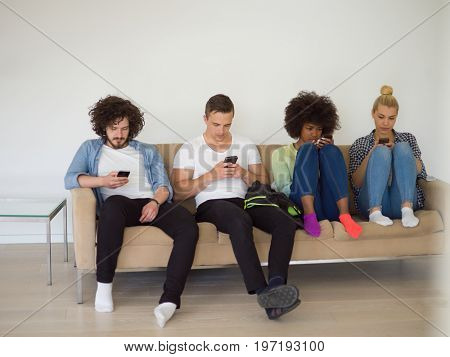 multiethnic group of young people sitting on a sofa at home, staring at smartphone, being antisocial, smartphone addiction