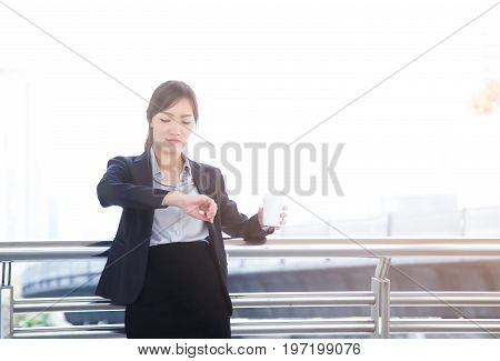 Beautiful business woman holding a cup of coffee and checking the time looking at his watch in the city street