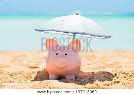 Pink Piggy Bank Under The Small Parasol During Summer At Beach