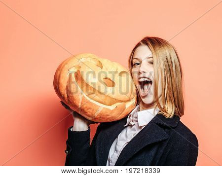 Halloween woman with happy face. Girl with scary pumpkin. Woman in coat and scarf at orange wall. Holiday and celebration. Party and traditional food.