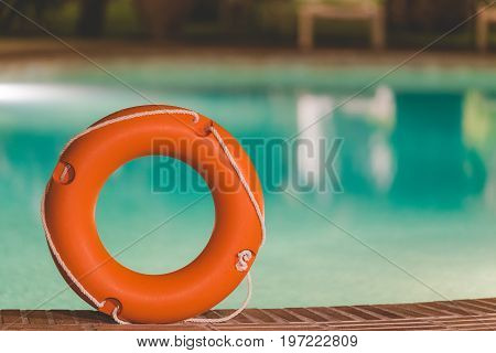 Orange lifebuoy or ring buoy on edge of swimming pool outdoors. Night scene.
