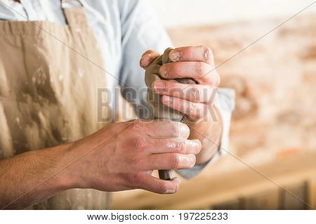 pottery, stoneware, ceramics art concept - closeup on master hands holding some piece of fireclay, young male in dirty apron work at a workshop, men hands form the future product from raw clay