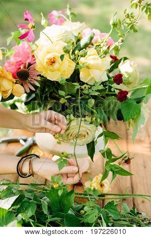 wedding, celebration, floral design, spring, nature concept - woman's hands fixing few stalks in great multicolored bouquet made of ballet pink peonies, english roses and avalanches