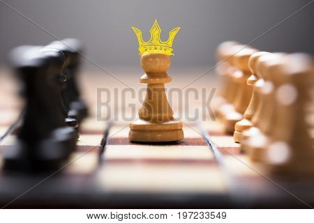 Closeup of pawn with king crown amidst chess pieces on board game representing leadership