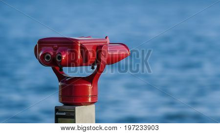 A red telescope on the shore of the lake constance in germany in front of blue water