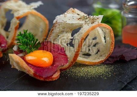 Cured meat on crusty bread with yolk and parmegano cheese, close view, selective focus.