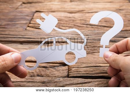 Cropped image of businessman holding paper electric car and question mark at wooden table