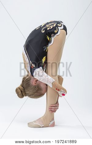 Caucasian Female Rhythmic Gymnast Athlete In Professional Competitive Suit Doing Backbend Stretching Exercise While Posing in Studio Against White. Vertical Composition