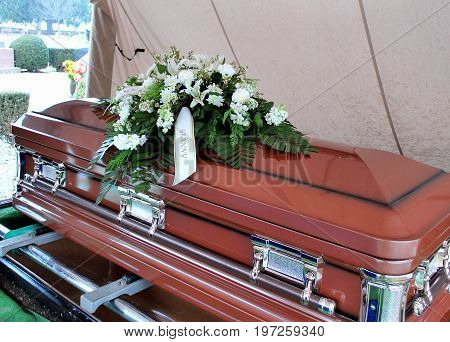 Casket at funeral service displayed outdoors with flowers.