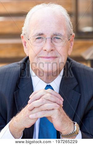 Closeup portrait of content senior business man looking at camera and keeping his hands clasped. Front view.