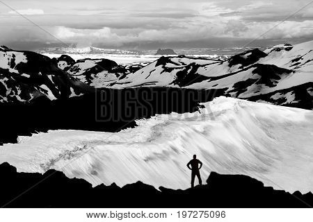 Man reaching mountain summit, watching glaciers and snowfields in Iceland. Unreal view from the volcano Ok with its snow-filled crater to the snowfields and glaciers of Thorisdalur. Large Langjokull glacier in background.