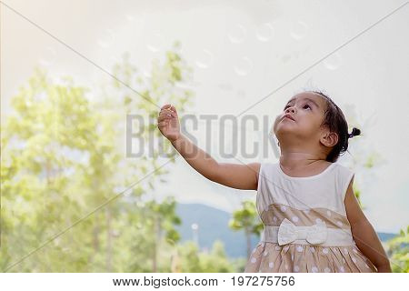 Happy child blowing soap bubbles in spring park with lens flares