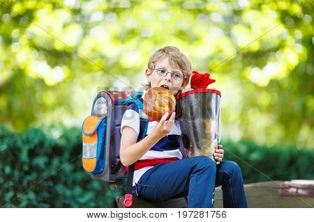 Happy little kid boy with glasses and backpack or satchel on his first day to school . Child outdoors on warm sunny day, Back to school concept. Kid with traditional schoolbag in German Schultuete