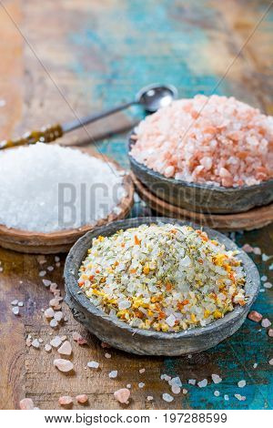 Different types of natural salt in stone bowls on wooden surface. White sea salt pink Himalayan salt Spiced salt with rosemary