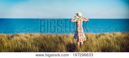 Summer Portrait Of Young Pretty Woman In A Straw Hat And Dress Standing Backwards In The Grass And L