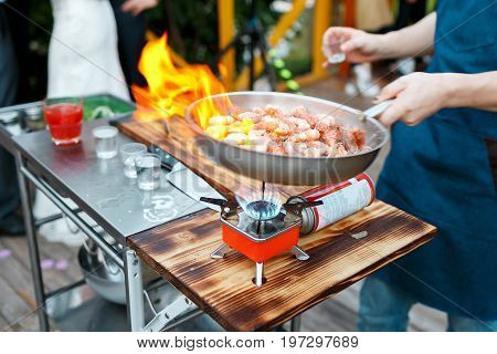 Fried king prawns on iron pan. the chef pours hot sauce. the bake outdoors on a portable gas burner
