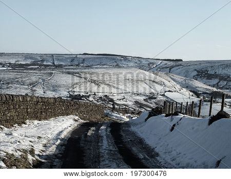 view of yorkshire moors covered in snow with a country road going downhill and the pennines on the horizon with paths and fields on a bright sunny day