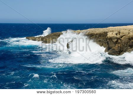 Wild waves of blue sea spatter on rocky shore of Gozo, Malta