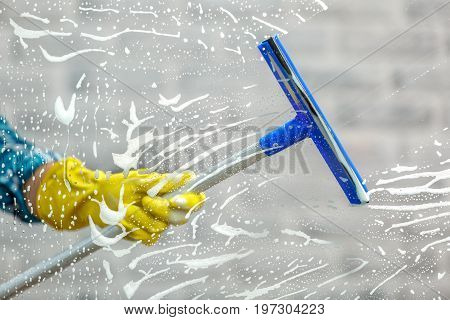 Studio shot through glass of housekeeper. Woman hand with glove holding squeegee for window. Focus on hand