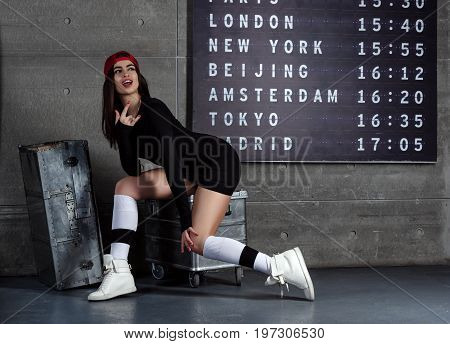 A cheerful girl - dancer sits on suitcases at the airport. Concept.