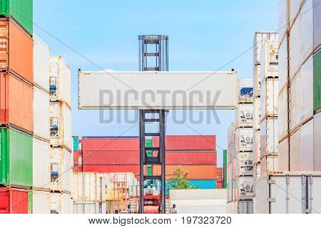 Forklift truck lifting cargo container in shipping yard or dock yard against blue sky cloudy with cargo container stack in background for transportation import Export and logistic industrial concept