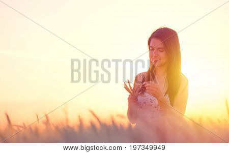 beautiful woman with a wheat bouguet in wheat field at sunset