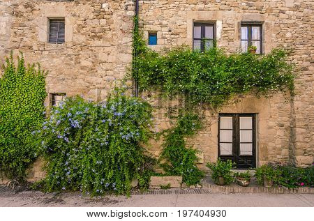 Windows on a stone and flowered facade in Peratallada. Peratallada is a picturesque medieval old town in the heart of Costa Brava, Catalonia, Spain.