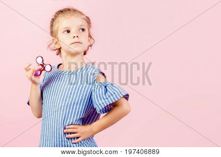 Little beautiful girl in blue stripped shirt is playing red spinner in hand