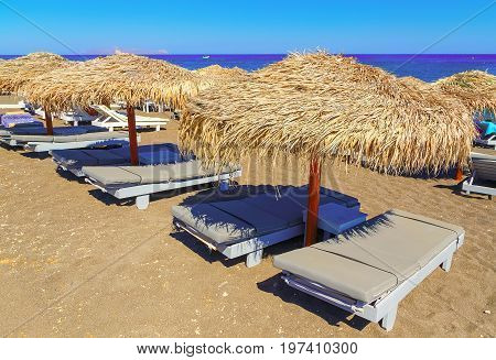 beach with straw umbrellas and wooden sunbeds on the island Satorini, Greece, Europe