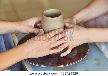 Hands of two people create pot on potter's wheel. Teaching pottery carftman's hands guiding