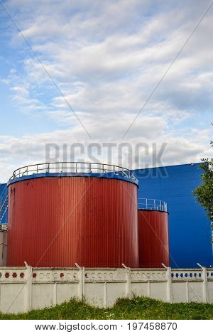 Large industrial tanks of red color against the blue industrial building