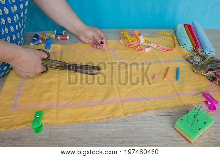 woman hands sewing yellow cloth outdoors. Tailor hands working with scissor and suit textile cloth