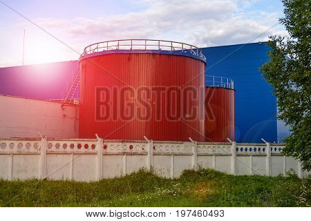 Large industrial tanks of red color against the blue industrial building