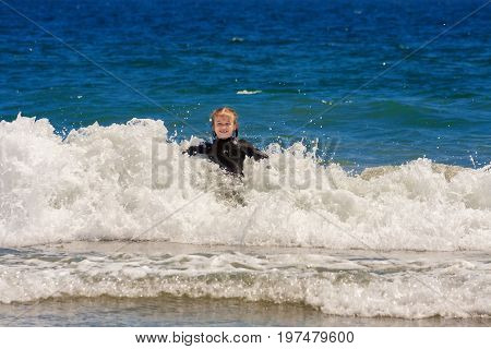A young girl plays in the ocean waves. She is leaning back into a breaking wave with white water on the crest. Her eyes are closed and she is laughing.