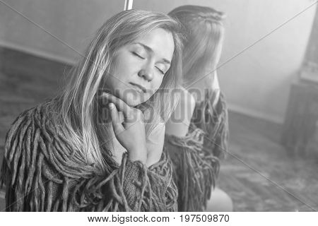 Tender close up black white sideways portrait of beautiful Caucasian woman with blond hair and soft skin with closed eyes enjoying bright light and warm sun from window indoors. Mirror reflection.