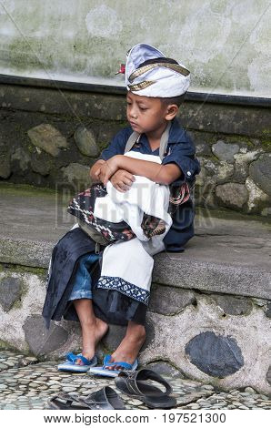 Ubud Bali Indonesia - July 30 2013. Portrait of sad unidentified boy sitting waiting for his family in the temple