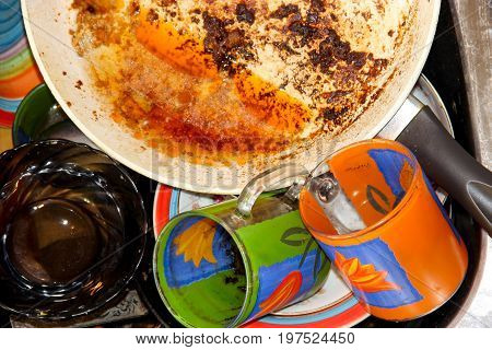 mass of dirty dishes with food scraps waiting to be washed in the metal sink