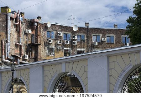Old brick facade of the house with air conditioning and satellite antennas for arched fence