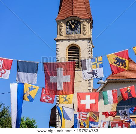 Wallisellen, Switzerland - 30 July, 2017: flags over Kirchstrasse street decorated for the upcoming Swiss National Day, selective focus on the foreground, the protestant church in the background. Wallisellen is a town in the Swiss canton of Zurich.