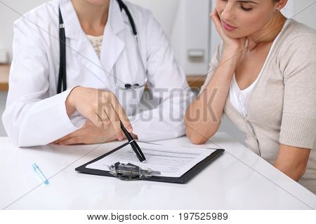Close up of doctor and patient sitting at the desk while physician pointing into medical form hystory. Medicine and health care concept.