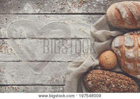 Love baking concept. Bread on rustic wood background, copy space. Brown and white loaves and flour still life composition with wheat flour sprinkled around.