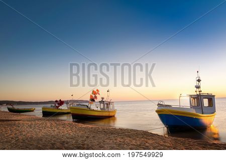 Sun just rises over colorful fishing cutters on sandy beach. Baltic sea Pomerania. Poland.