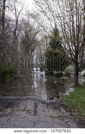 Vertical of flood waters rising over a paved road with trees and foliage partly submerged in the West Island of Montreal, Quebec on a bright overcast day in May.