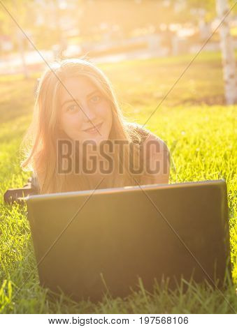 Young woman using laptop in the park lying on the green grass. Leisure time activity concept.