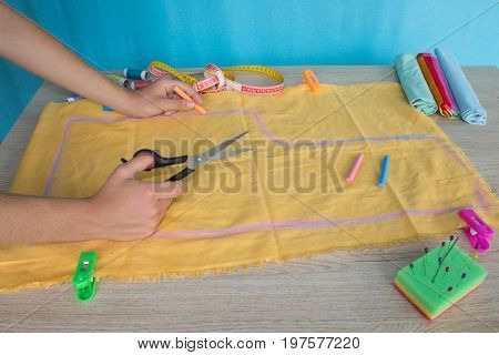 Tailor cutting fabric using large scissors or shears as he follows the chalk markings of the pattern close up of his hands. Woman's Hand Sewing Quilt