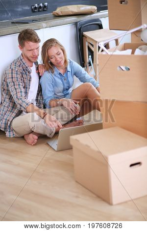 Young couple moving in new home.Sitting and relaxing after unpacking.Looking something on laptop. Young couple