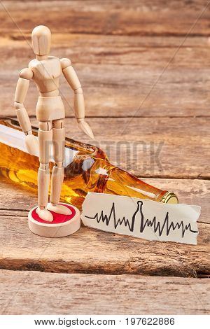 Human wooden dummy standing near alcohol. Wooden human figure, bottle of alcohol, wooden background. Alcohol harm health.