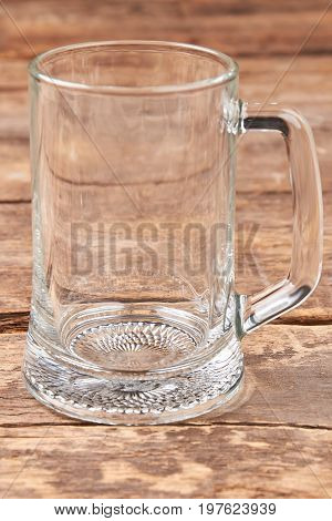 Empty beer mug isolated on wooden background. Transparent glass container for beer, old wooden table.