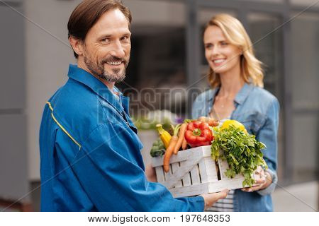 Providing services. Handsome gallant energetic man meeting young lady while doing his job and delivering products from vegetable store